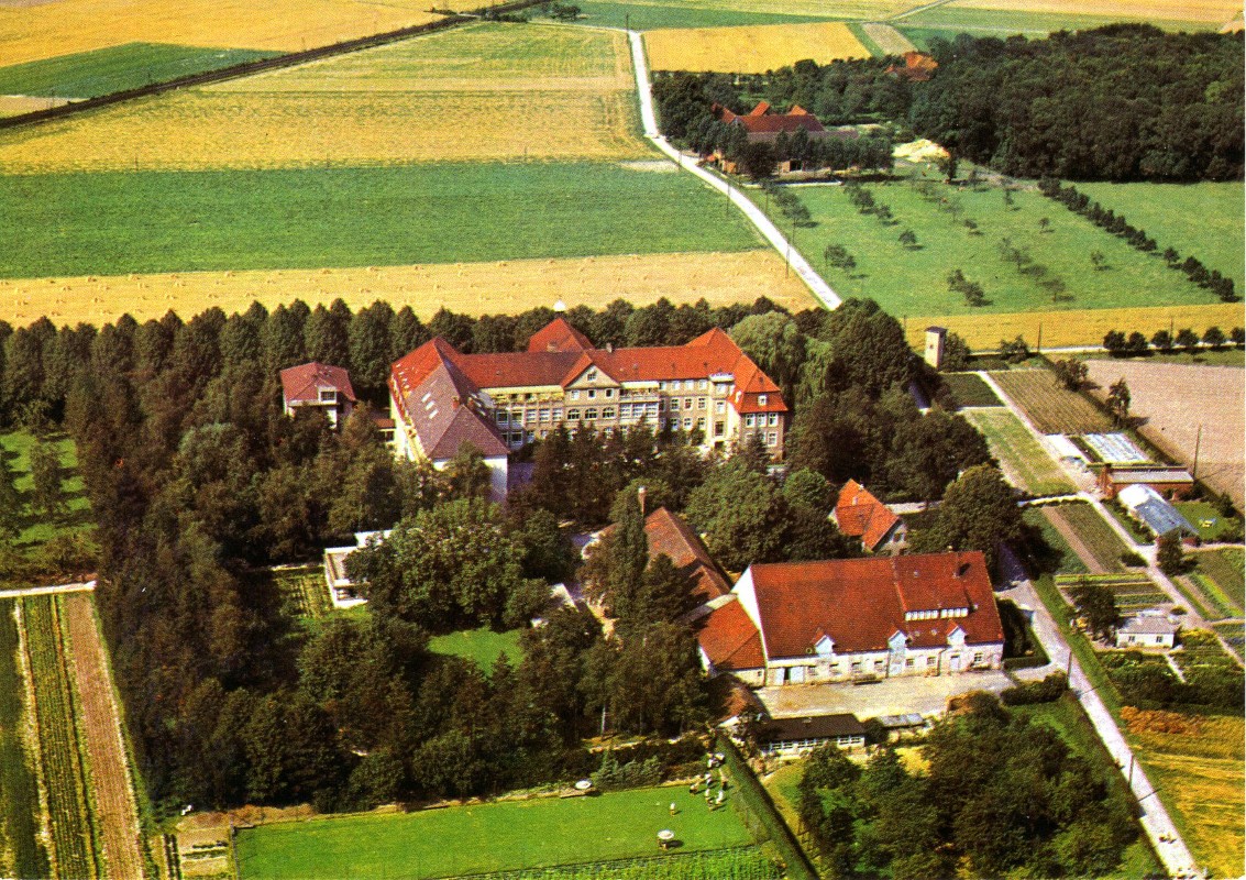 Luftaufnahme eines ländlichen Gutshofs mit roten Dächern, umgeben von Bäumen, Feldern und landwirtschaftlichen Parzellen